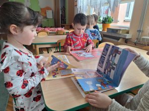Dzieci siedzą przy stole i oglądają wybrane książki.