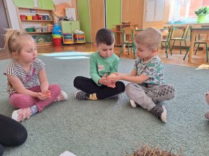 Dzieci siedzą w kole na dywanie, podają sobie jajko z rąk do rąk.