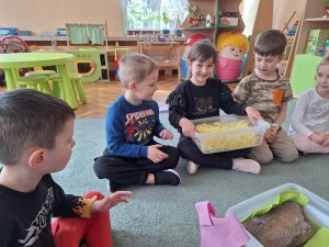 Dzieci siedzą na dywanie.  Oglądają imitację siana w pudełku.