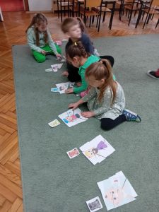 Dzieci siedzą na dywanie i dopasowują do obrazków przedstawiających kosze pasujące do nich obrazki ułożone wcześniej z puzzli.