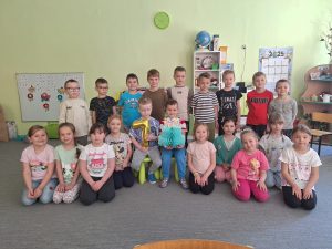 Grupa dzieci pozuje do pamiątkowego zdjęcia z okazji urodzin dwóch chłopców. Solenizanci siedzą na środku, otaczają ich rówieśnicy.