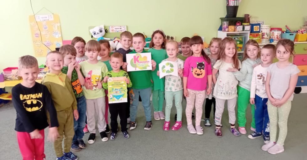 Dzieci stoją obok siebie. Trójka z nich trzyma obrazki związane z realizacją "Misji recykling" z programu "Kubusiowi przyjaciele natury".