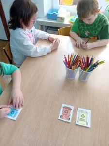 Dzieci siedzą przy stoliku I kolorują obrazki przedstawiające kosze na śmieci.