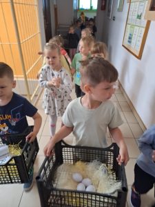 Chłopiec niesie skrzynkę wypełnioną sztucznym siankiem i plastikowymi jajkami.