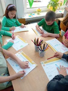 Dzieci siedzą przy stolikach i łączą z plastikową butelką inne plastikowe przedmioty.