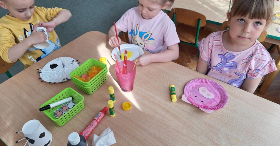 Troje dzieci siedzi przy stole. Wykonują pracę plastyczną.