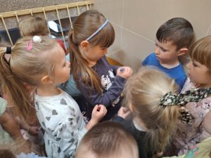Dziewczynka rozwija kartkę z ukrytą zagadką. Dzieci stoją wokół i przyglądają się.