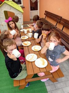 Dzieci siedzą przy stolikach na tarasie i jedzą mango.
