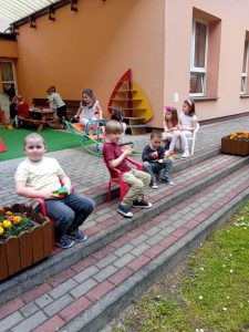 Chłopcy siedzą na krzesłach na schodach tarasu i korzystają z promieni słonecznych.
