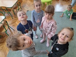 Grupka dzieci stoi w kółeczku. Na szyi mają emblematy ze świnkami.