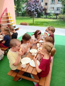 Dzieci siedzą przy stolikach na tarasie i jedzą mango.
