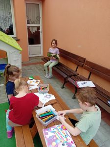 Dzieci siedzą przy stolikach na tarasie I rysują dowolne obrazki.
