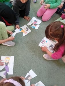 Dzieci układają na dywanie papierowe puzzle.