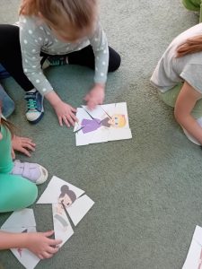 Dzieci układają na dywanie papierowe puzzle.
