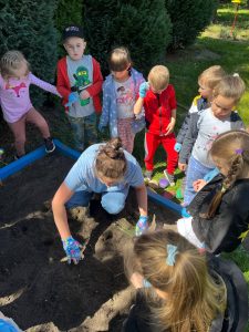 Dzieci stoją wokół pani w ogródku.