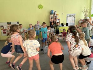 Solenizant stoi w środku,  wokół niego w kole rówieśnicy z grupy. dzieci skaczą.