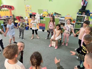 Dziewczynka siedzi na środku. Rówieśnicy stoją wokół i śpiewają urodzinową piosenkę.
